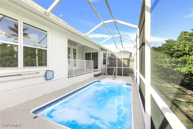 view of pool featuring ceiling fan, glass enclosure, a shed, and a patio area