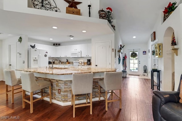 kitchen with a kitchen bar, light stone counters, white cabinets, and white appliances