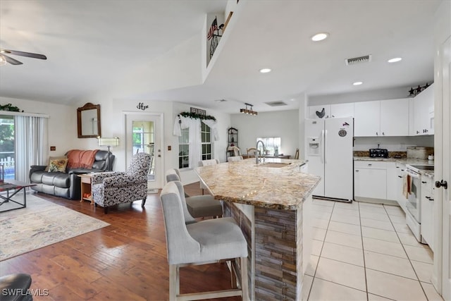 kitchen featuring a kitchen breakfast bar, white appliances, a kitchen island with sink, sink, and white cabinetry