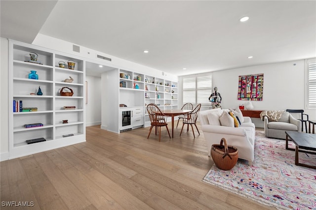 living room featuring built in shelves, light hardwood / wood-style floors, and beverage cooler