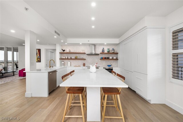 kitchen with a kitchen bar, kitchen peninsula, wall chimney exhaust hood, dishwasher, and white cabinetry