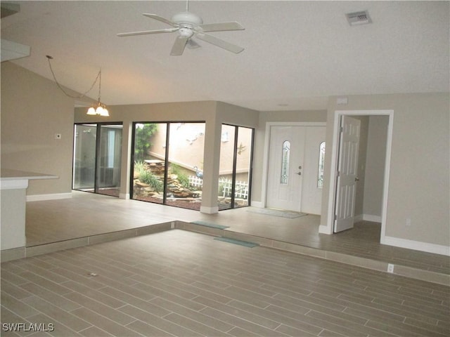 unfurnished living room featuring ceiling fan with notable chandelier, wood-type flooring, and vaulted ceiling