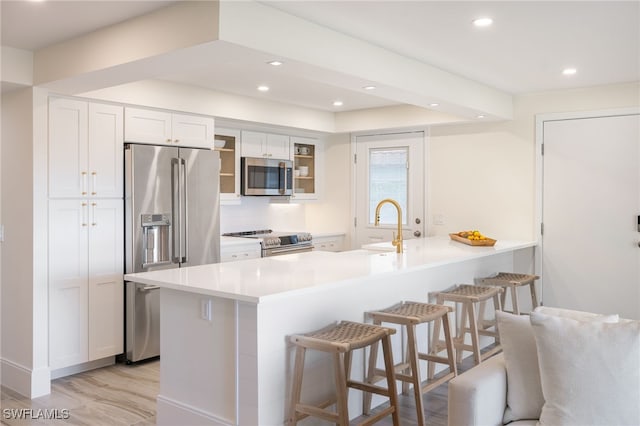 kitchen featuring stainless steel appliances, sink, light hardwood / wood-style flooring, white cabinetry, and a breakfast bar area