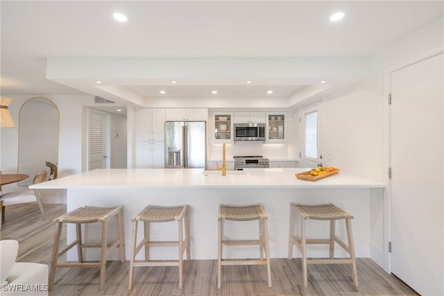 kitchen featuring sink, premium appliances, kitchen peninsula, white cabinets, and light wood-type flooring