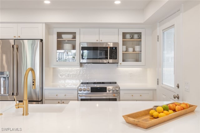 kitchen featuring a healthy amount of sunlight, high end appliances, white cabinetry, and tasteful backsplash