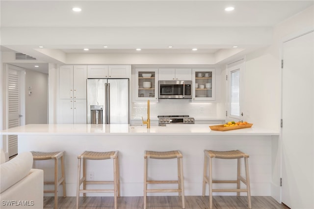 kitchen with a kitchen bar, kitchen peninsula, stainless steel appliances, and white cabinetry