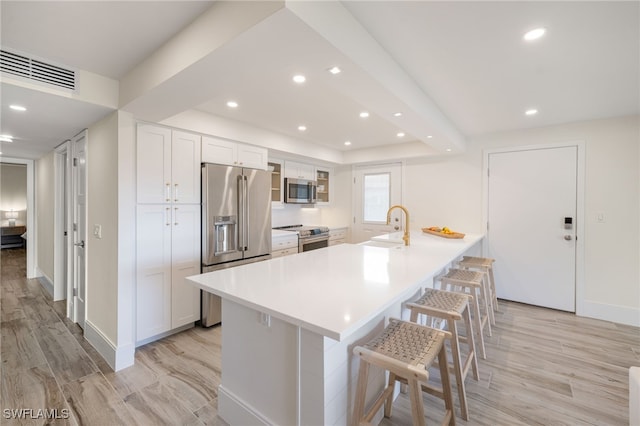 kitchen with a kitchen bar, a large island with sink, white cabinets, and stainless steel appliances