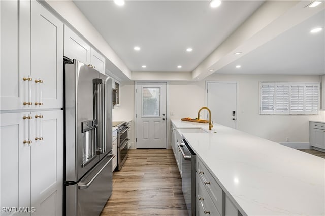 kitchen featuring sink, light stone countertops, light wood-type flooring, white cabinetry, and stainless steel appliances