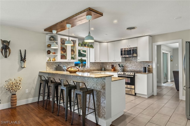 kitchen featuring stainless steel appliances, white cabinetry, kitchen peninsula, and decorative light fixtures