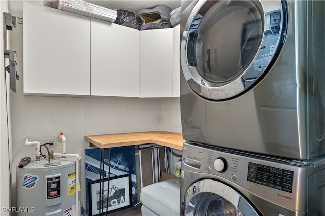 washroom with stacked washing maching and dryer, cabinets, and electric water heater