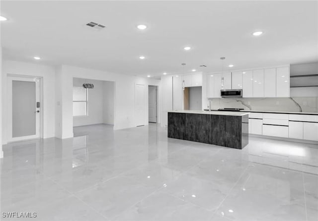 kitchen featuring tasteful backsplash, white cabinetry, an island with sink, and decorative light fixtures