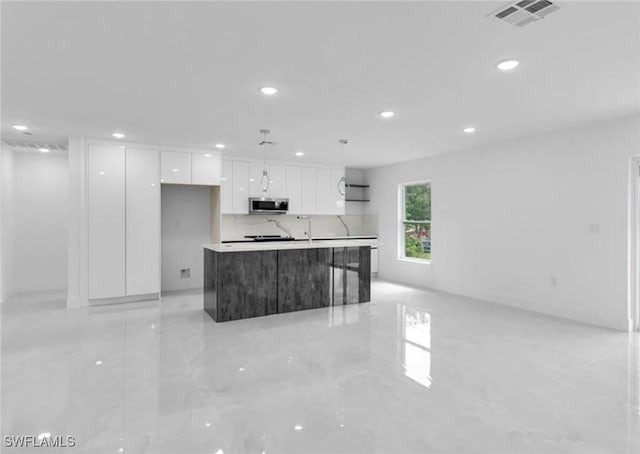 kitchen with pendant lighting, backsplash, white cabinetry, and a kitchen island with sink