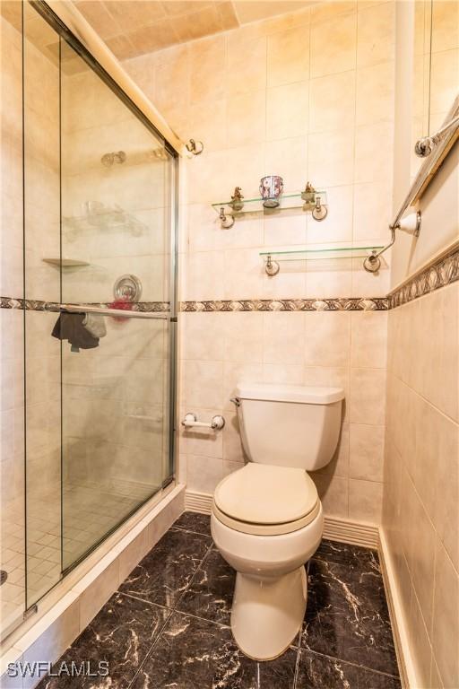 bathroom with toilet, walk in shower, and tile walls