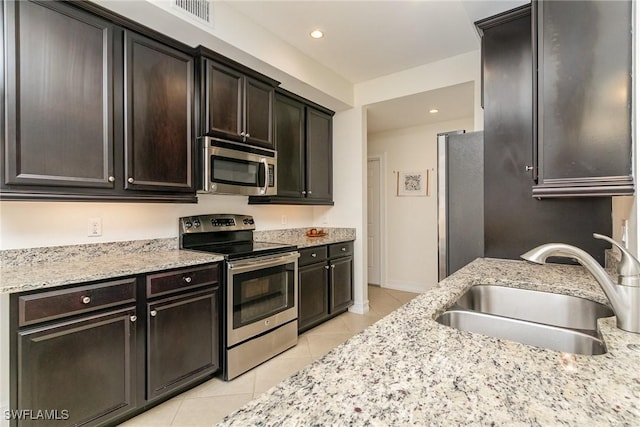 kitchen with appliances with stainless steel finishes, dark brown cabinetry, light tile patterned floors, and sink