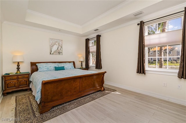 bedroom featuring a tray ceiling, light hardwood / wood-style flooring, and multiple windows