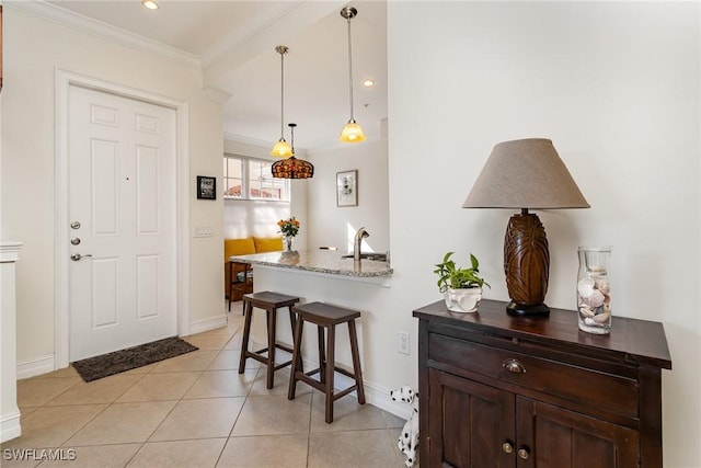 kitchen featuring pendant lighting, a breakfast bar, crown molding, light stone countertops, and light tile patterned floors