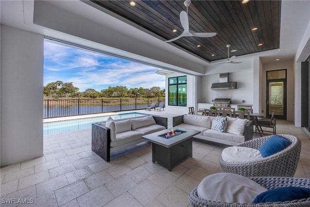 view of patio / terrace featuring ceiling fan, an outdoor kitchen, a grill, an outdoor living space with a fire pit, and a water view