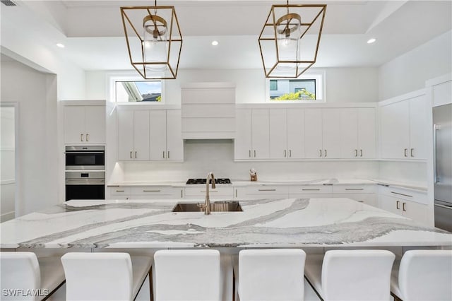 kitchen featuring sink, decorative light fixtures, a breakfast bar area, a kitchen island with sink, and white cabinets