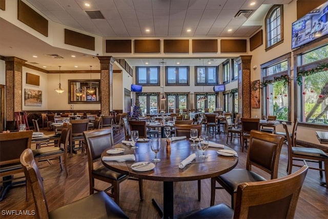 dining space featuring ornate columns, a towering ceiling, a healthy amount of sunlight, and hardwood / wood-style flooring