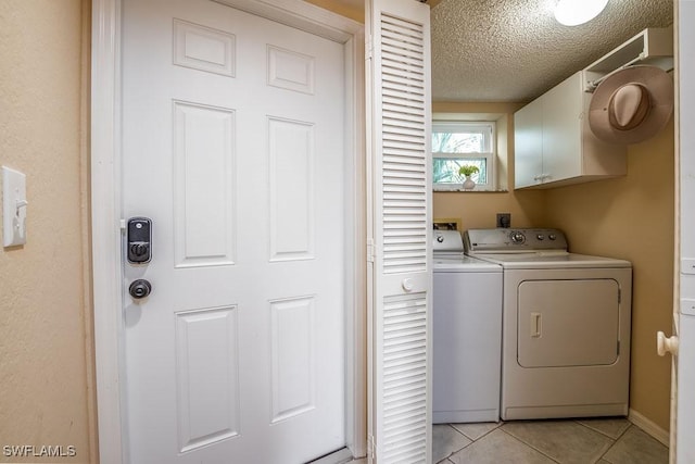 clothes washing area with light tile patterned floors, a textured ceiling, cabinet space, and washer and dryer