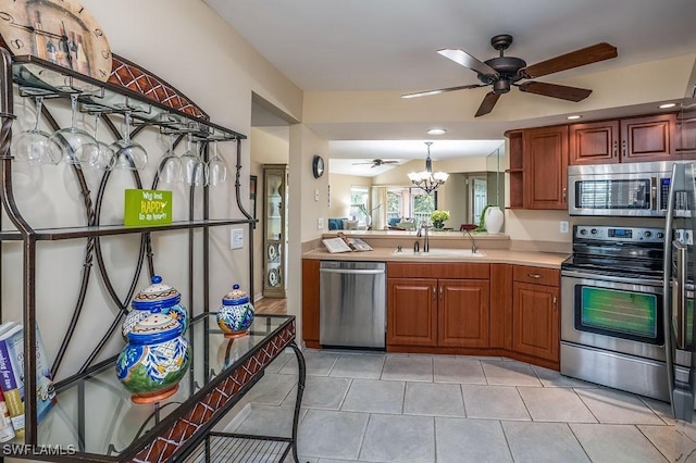 kitchen featuring light tile patterned floors, stainless steel appliances, light countertops, a sink, and ceiling fan with notable chandelier