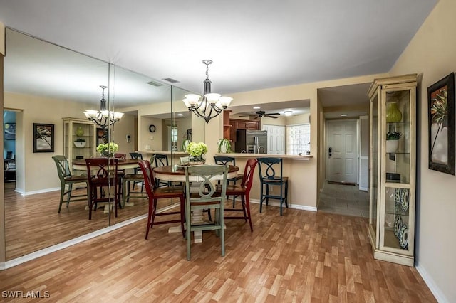 dining space with ceiling fan with notable chandelier, light wood-type flooring, and baseboards