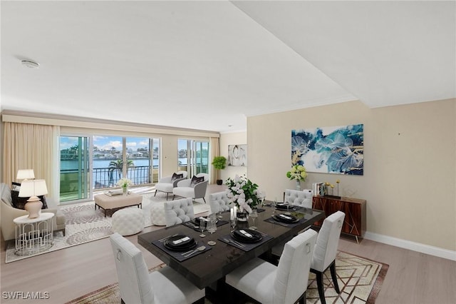 dining area featuring light wood-type flooring, a water view, crown molding, and baseboards