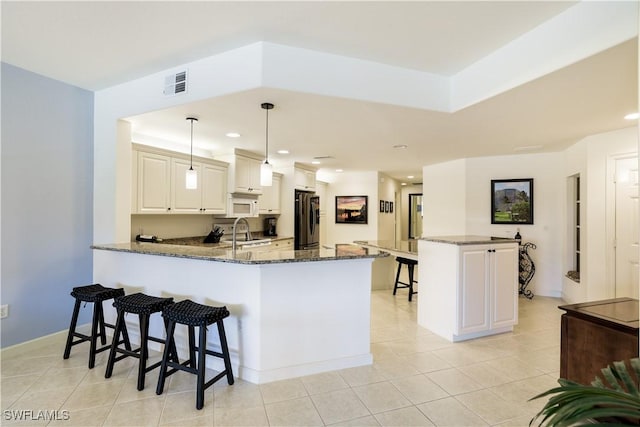 kitchen featuring sink, stainless steel fridge with ice dispenser, kitchen peninsula, dark stone counters, and pendant lighting