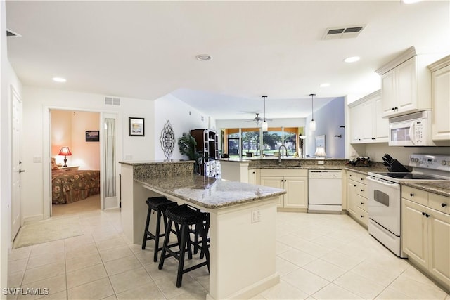 kitchen with white appliances, stone counters, kitchen peninsula, hanging light fixtures, and a breakfast bar area