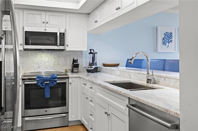 kitchen featuring appliances with stainless steel finishes, white cabinetry, a sink, and light stone counters