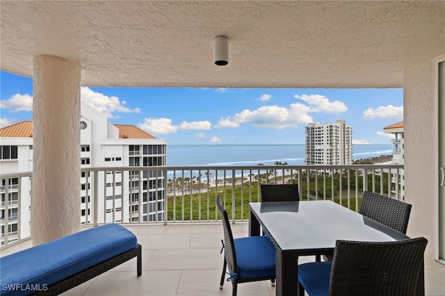 balcony with outdoor dining area, a water view, and a view of the beach