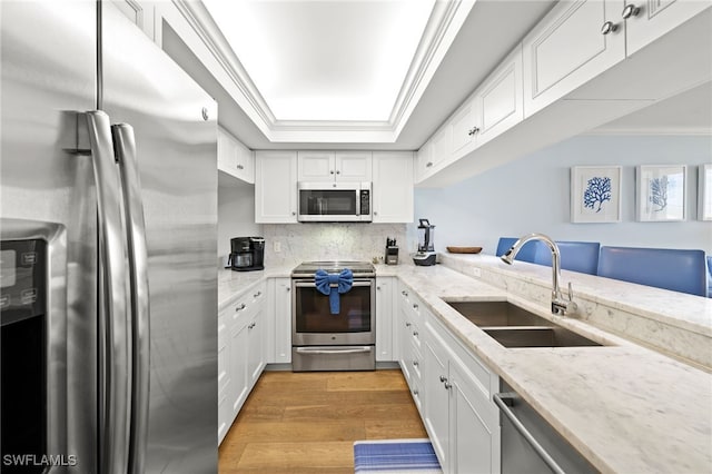 kitchen with stainless steel appliances, white cabinetry, a sink, and crown molding