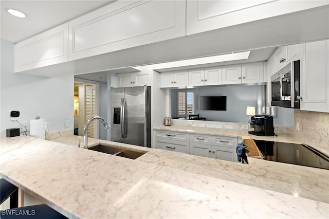 kitchen featuring stainless steel appliances, light stone counters, a sink, and white cabinetry