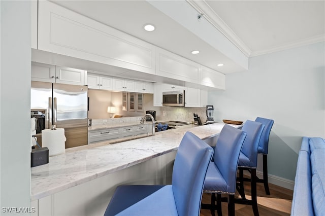 kitchen featuring a peninsula, a kitchen bar, appliances with stainless steel finishes, and white cabinets