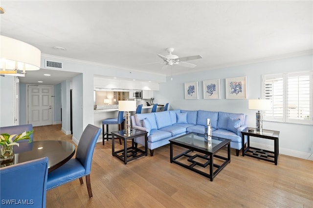 living room with ceiling fan, visible vents, baseboards, ornamental molding, and light wood-type flooring