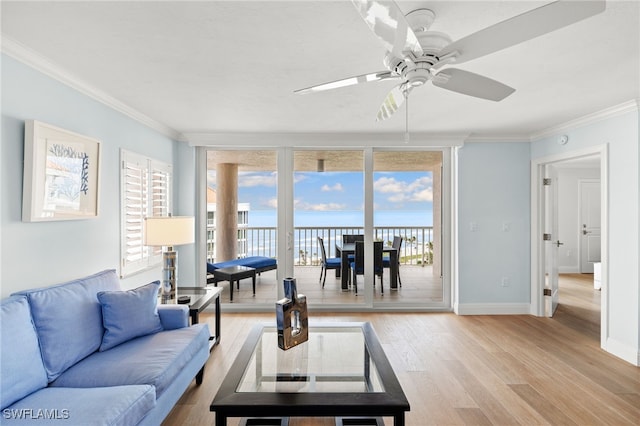 living area featuring light wood-style flooring, a water view, baseboards, ornamental molding, and expansive windows