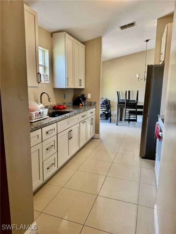 kitchen featuring pendant lighting, sink, stainless steel fridge, light stone counters, and light tile patterned floors