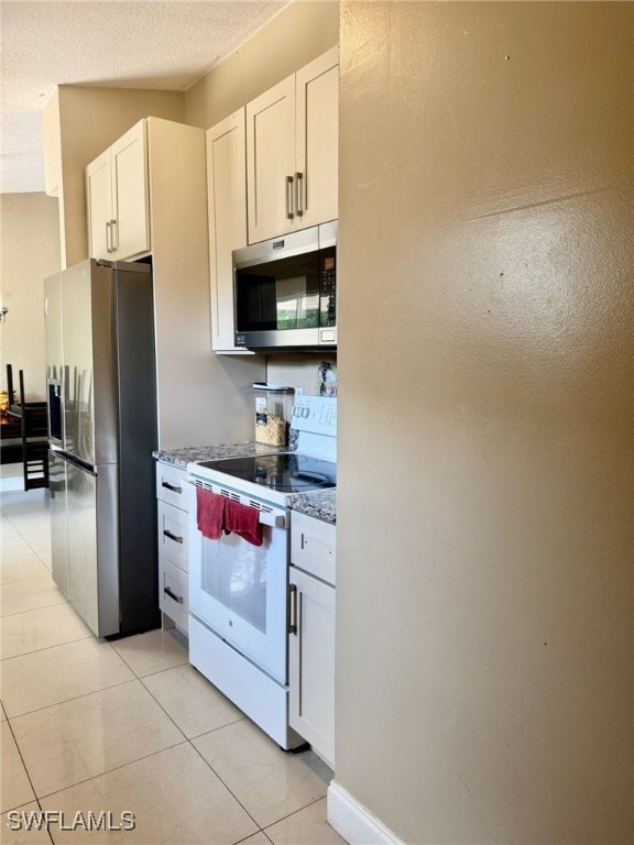 kitchen featuring light tile patterned floors, white cabinetry, appliances with stainless steel finishes, and stone counters