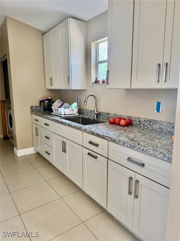 kitchen featuring washer / clothes dryer, sink, light tile patterned floors, light stone countertops, and white cabinets