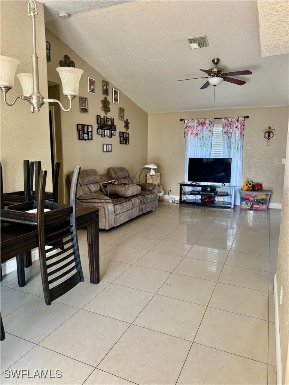 tiled living room featuring vaulted ceiling, ceiling fan, and a textured ceiling