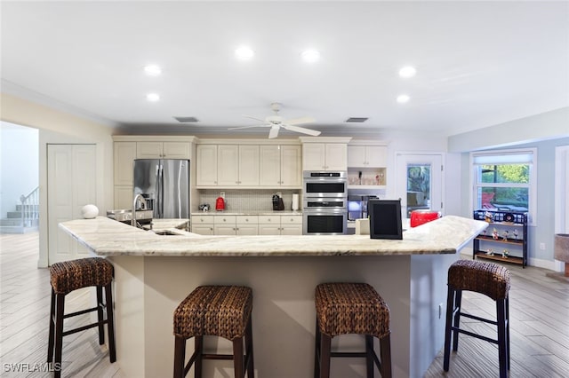 kitchen featuring backsplash, a kitchen breakfast bar, a large island with sink, and appliances with stainless steel finishes