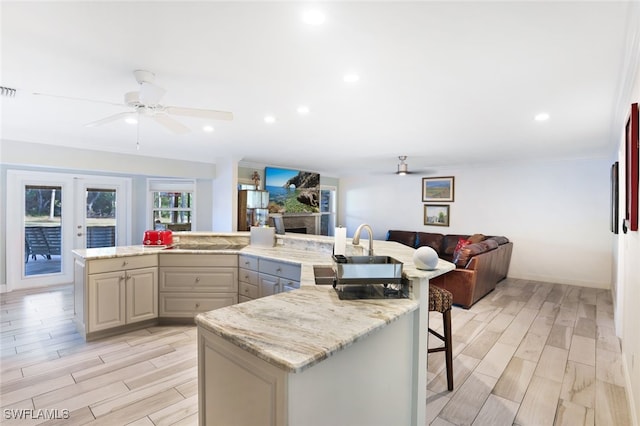 kitchen with a kitchen bar, light wood-type flooring, light stone countertops, and sink