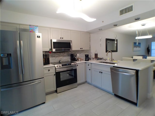 kitchen featuring kitchen peninsula, backsplash, stainless steel appliances, sink, and hanging light fixtures