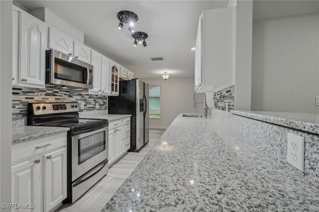 kitchen with white cabinetry, appliances with stainless steel finishes, tasteful backsplash, light stone countertops, and sink