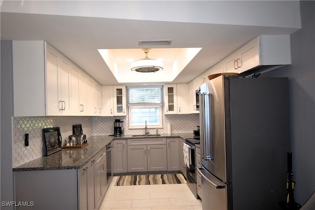 kitchen with appliances with stainless steel finishes, a tray ceiling, sink, dark stone countertops, and white cabinets