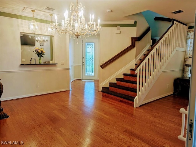 foyer entrance with hardwood / wood-style floors, ornamental molding, and a notable chandelier