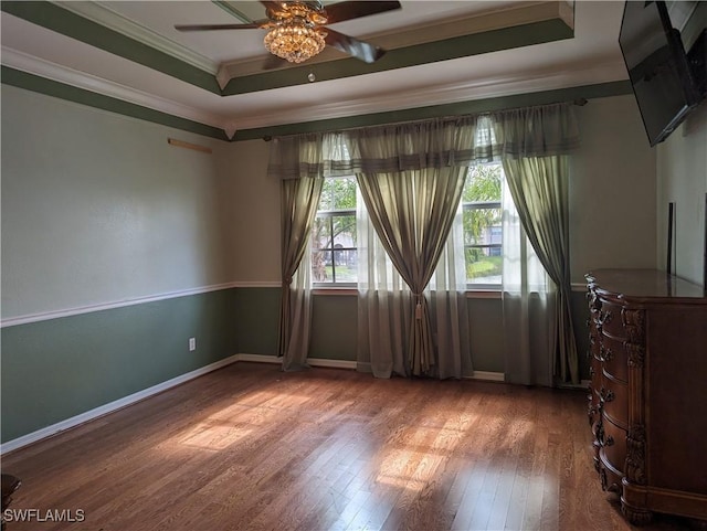 empty room featuring hardwood / wood-style flooring, ceiling fan, crown molding, and a tray ceiling