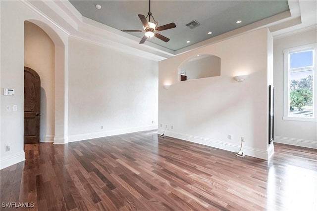 empty room with a raised ceiling, ceiling fan, dark wood-type flooring, and ornamental molding