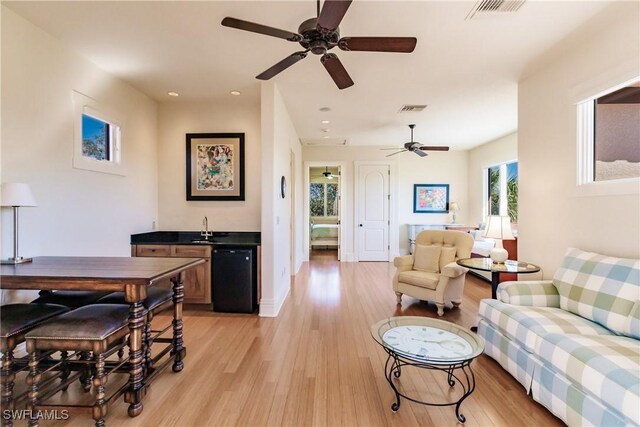 living room with light wood-type flooring, ceiling fan, and sink