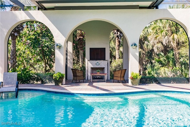 view of swimming pool featuring a patio and exterior fireplace